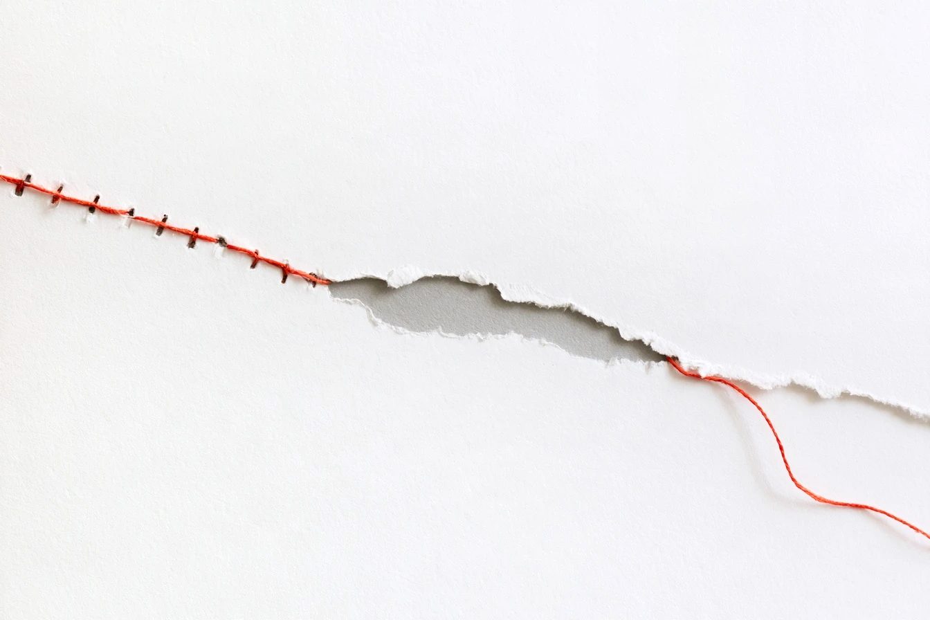 A single crimson thread running in a long ridge across white paper