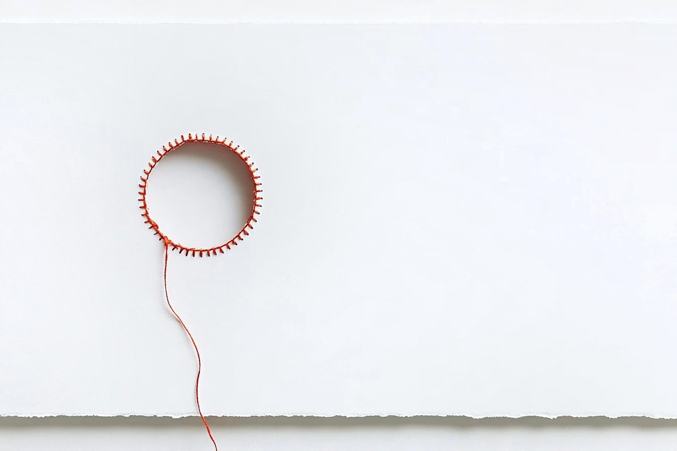 An orange-red thread stitched in a circle with a gap, its tail running down the sheet